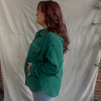 Person wearing a green jacket standing against a plain white backdrop