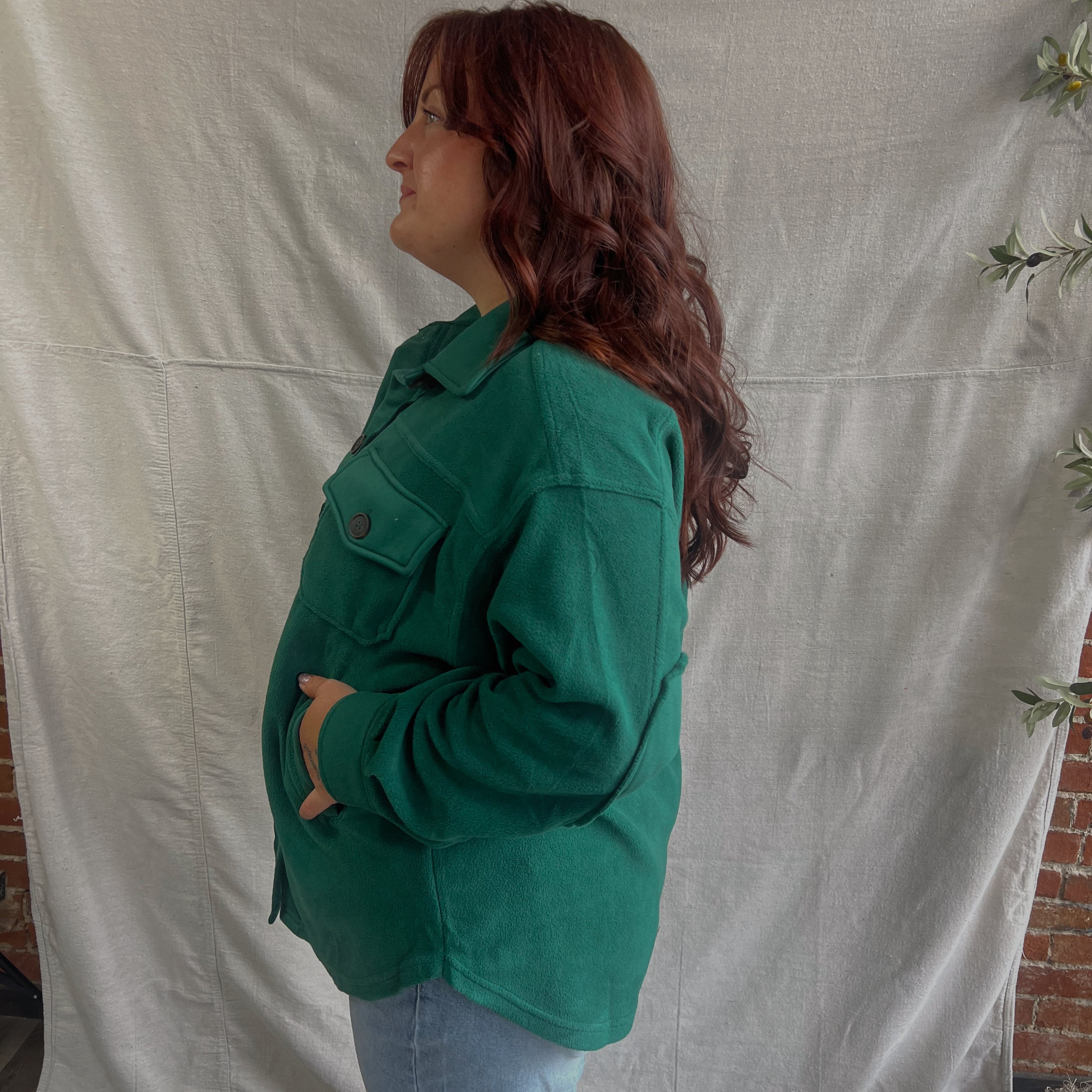 Person wearing a green jacket standing against a plain white backdrop