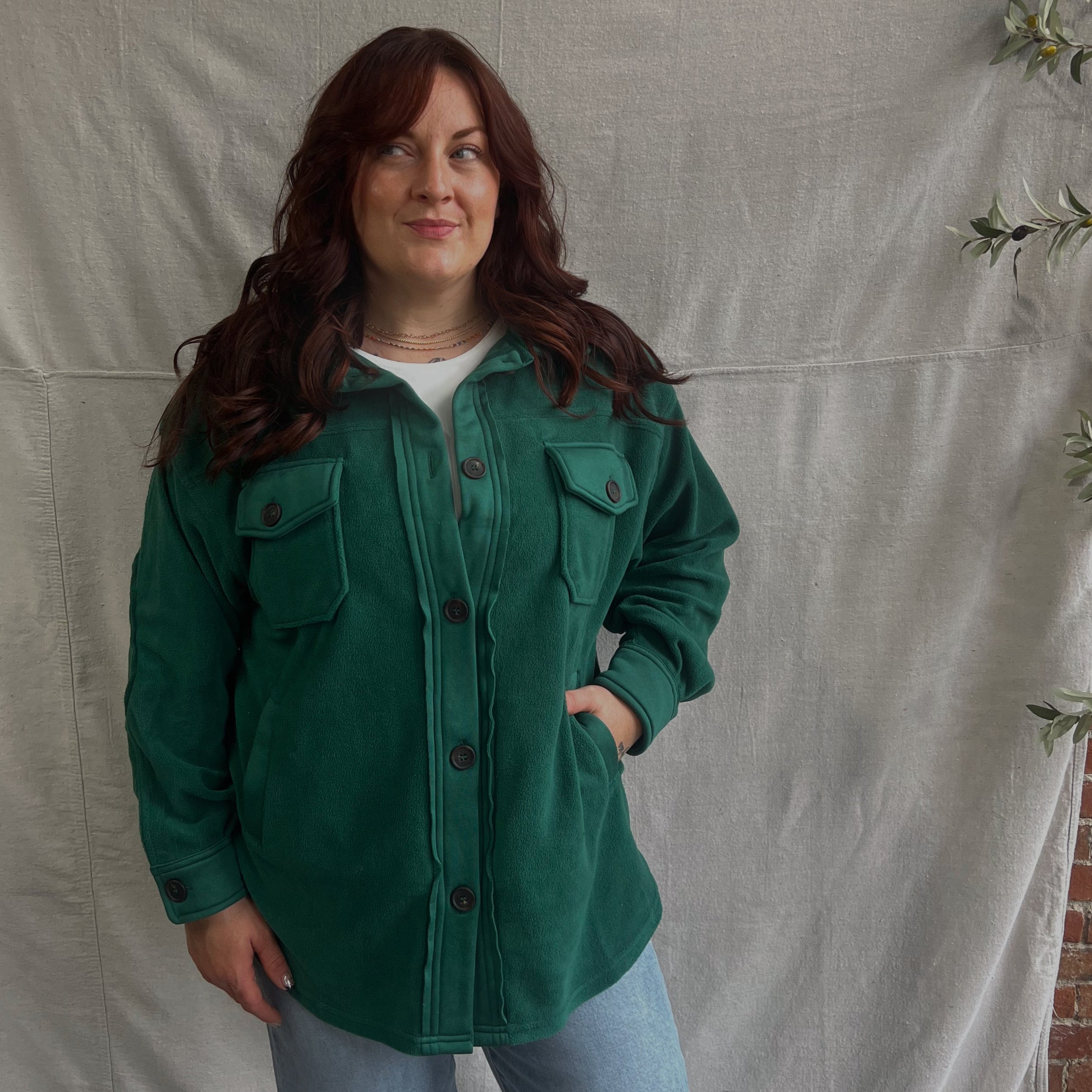 Person wearing a green jacket standing in front of a white backdrop with a brick wall background
