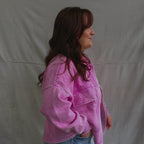 Person wearing a pink jacket and blue jeans standing against a plain background