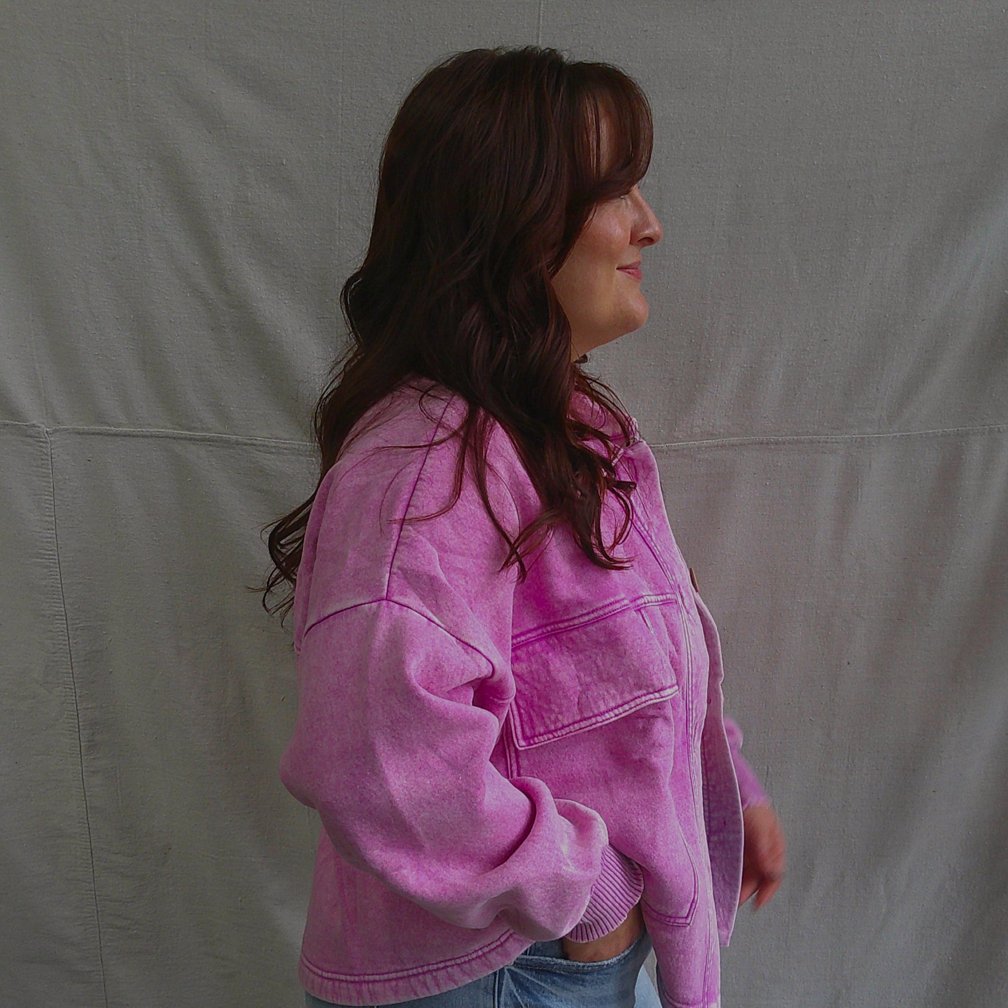 Person wearing a pink jacket and blue jeans standing against a plain background